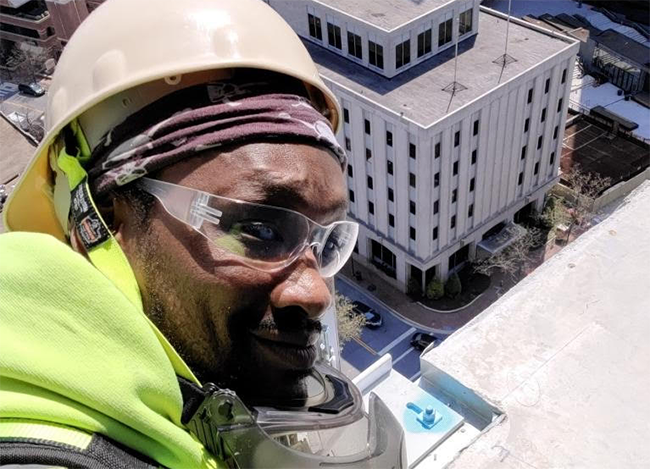 John wears protective glasses and hard hat on the roof of a building